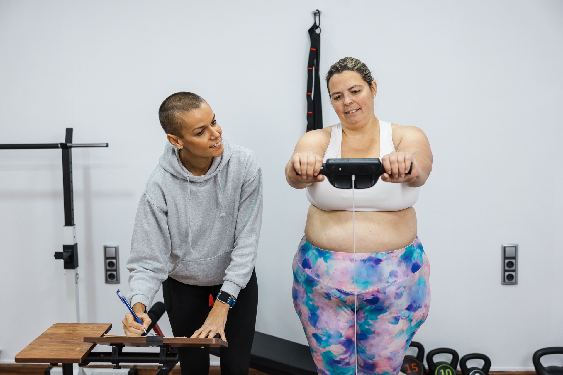 Nutritionist taking notes while client weighs herself on smart scale in gym
