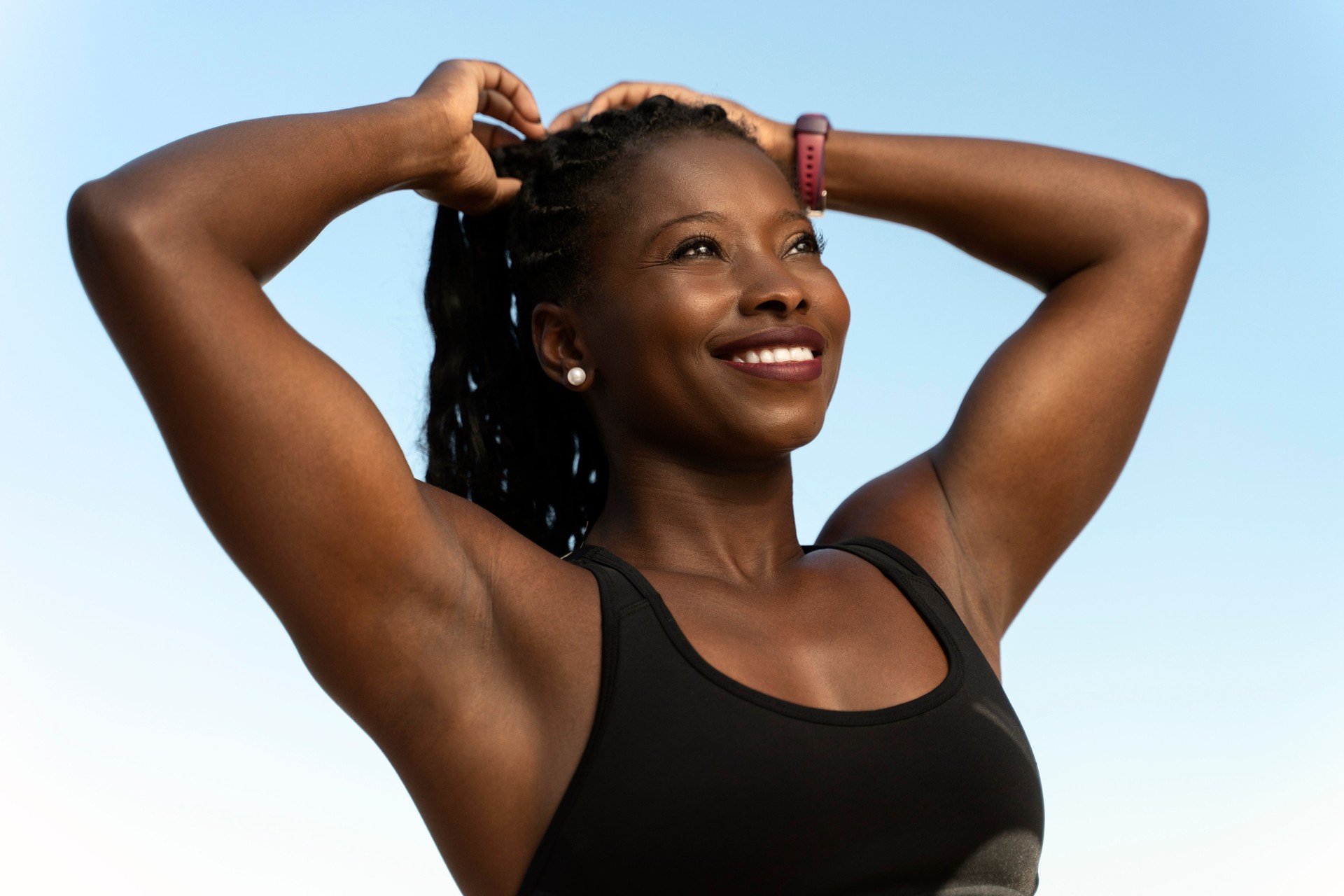 Multiracial woman smiling positively and making ponytail while looking at the distance
